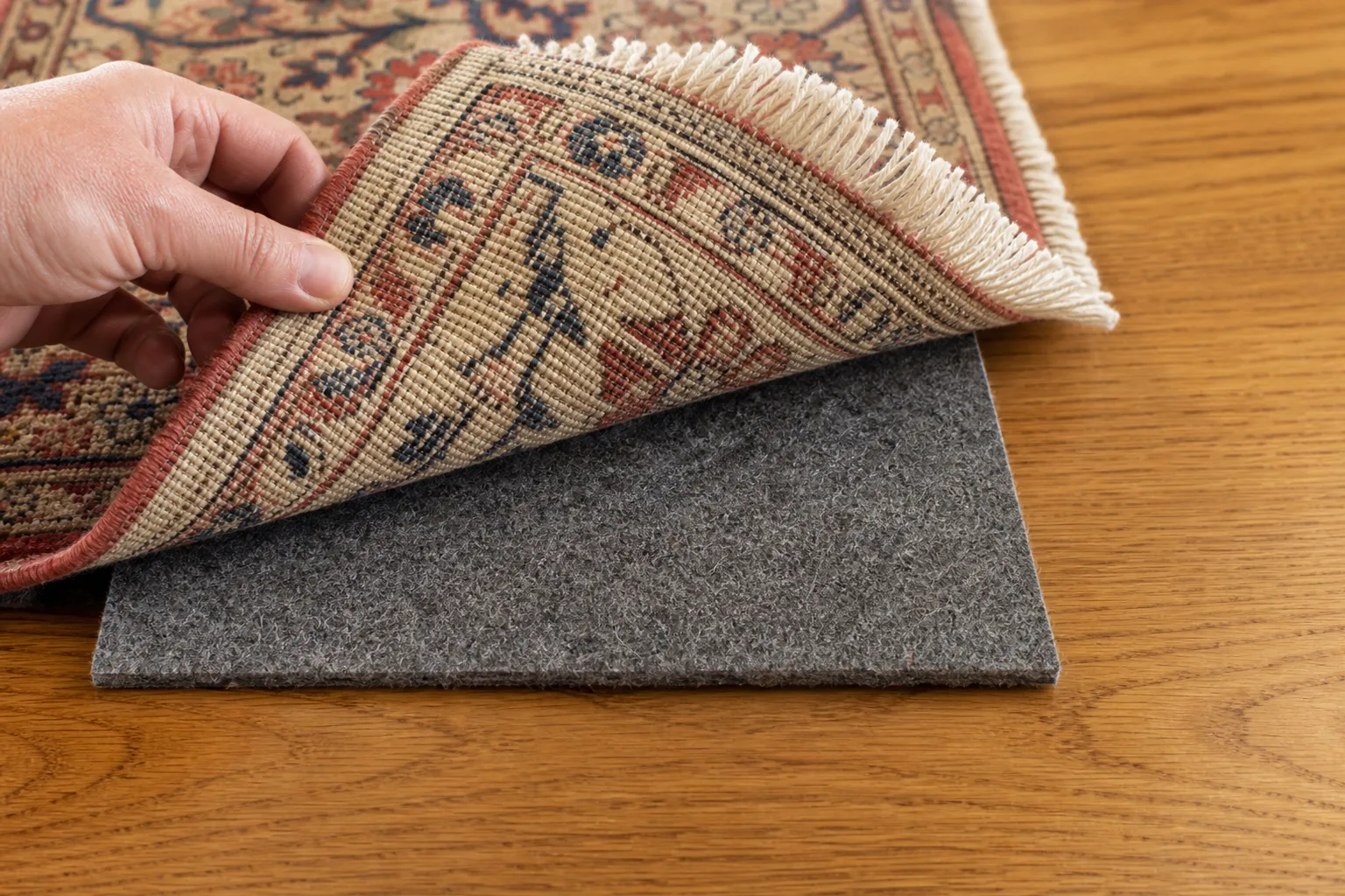 Close view of a hand-knotted rug reverse, one low felt rug pad and a wooden floor with the pad correctly inset from the edge